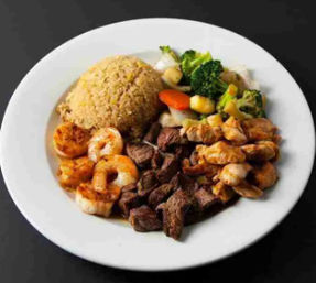 Surf-and-turf plate with a mound of fried rice, grilled shrimp, cubed steak, sliced chicken and stir-fried vegetables (broccoli, carrots) on a white plate