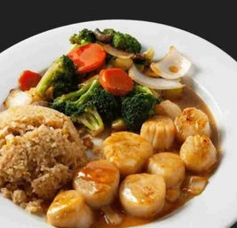 Pan-seared scallops in a savory brown sauce with fried rice and broccoli-carrot stir-fry on a white plate — Asian-inspired seafood entrée.