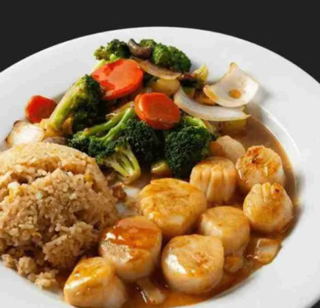 Pan-seared scallops in a savory brown sauce with fried rice and broccoli-carrot stir-fry on a white plate — Asian-inspired seafood entrée.