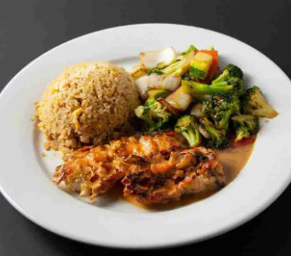 Glazed grilled chicken with fried rice and vibrant stir-fried broccoli, carrots, and onions served on a white plate.