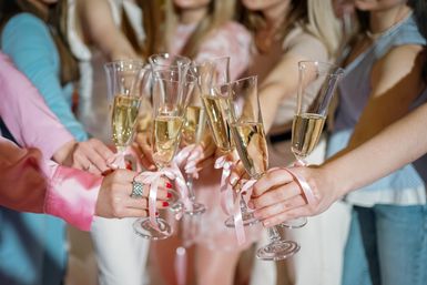 Close-up of women toasting with champagne flutes tied with pink ribbons, a festive bachelorette or bridal shower celebration.