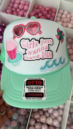 Mint green foam-front trucker hat with embroidered patches: sequin heart sunglasses, popsicle float, pinwheel, teal waves, and pink embroidered slogan "Girls just wanna have fun", shown over trays of pink craft beads.