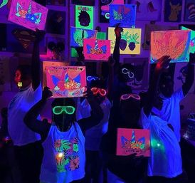 Children holding neon unicorn paintings under blacklight in a dark room, wearing glowing neon sunglasses and fluorescent white shirts for a glow-art party.