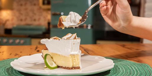 Toasted meringue key lime pie slice with lime wedge on a white plate, spoon lifting a bite in a cozy retro-style kitchen setting