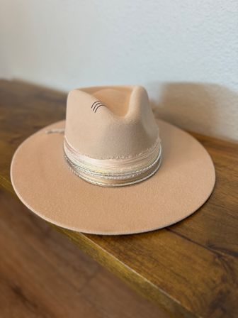Chic tan wool-felt wide-brim fedora with layered braided hatband resting on a wooden table against a white wall