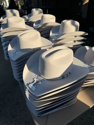 Rows of sunlit white felt cowboy hats stacked on an outdoor western market display.