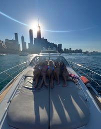 Group of five people lounging on a yacht bow with the Chicago skyline and sunburst over a downtown skyscraper, cruising Lake Michigan on a summer day