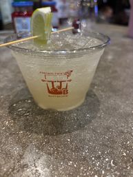 Fizzy lime cocktail in a plastic cup with crushed ice and a lime wedge on a toothpick, sitting on a speckled bar countertop.