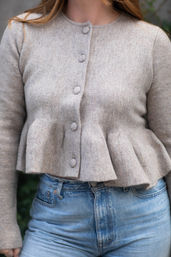 Close-up of a neutral beige knit peplum cardigan with fabric-covered buttons paired with high-waist light blue jeans — casual street-style outfit.