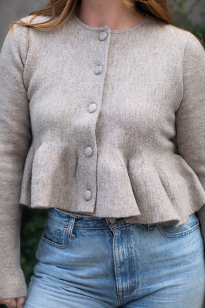 Close-up of a neutral beige knit peplum cardigan with fabric-covered buttons paired with high-waist light blue jeans — casual street-style outfit.