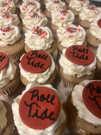 Close-up of mini vanilla cupcakes with swirled white buttercream, red fondant discs hand-lettered 'Roll Tide' and red-and-white sprinkle confetti