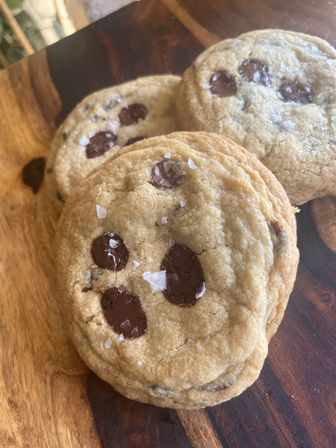 Close-up of freshly baked chocolate chip cookies with melted chocolate chips and flaky sea salt on a wooden cutting board