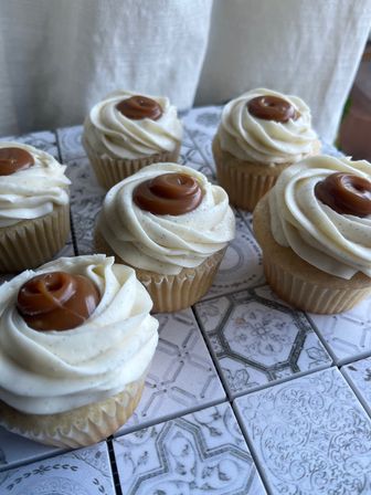 Close-up of vanilla cupcakes with piped vanilla buttercream swirls topped with caramel rosettes, arranged on decorative vintage tile surface