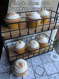 Rustic two-tier wire stand of pumpkin cupcakes topped with creamy swirls of cream-cheese frosting and a cinnamon dusting on patterned tile countertop — bakery-style display.