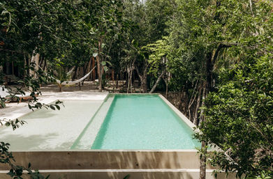 Secluded raised rectangular turquoise plunge pool with shallow wading ledge, hammock and sandy lounge area tucked into a dense tropical forest retreat