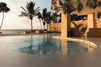 Serene sunset beachfront infinity pool with open-air lounge, swaying palm trees and ocean view at a tropical resort