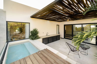 Modern rooftop terrace with private plunge pool, wooden deck, slatted pergola, outdoor sink and counter, black wire lounge chairs, sliding glass doors and tropical plants.