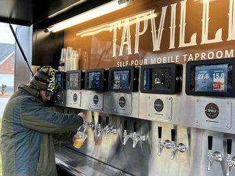 Customer in a winter jacket pouring draft beer from a self-serve mobile tap trailer with touchscreen pour displays