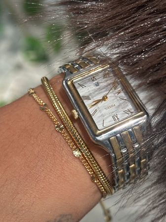 Chic close-up of a wrist wearing a two-tone rectangular watch with Roman numerals, paired with stacked gold bracelets
