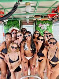 Smiling group of women in bikinis and heart-shaped sunglasses posing on a covered summer party boat cruising on calm water
