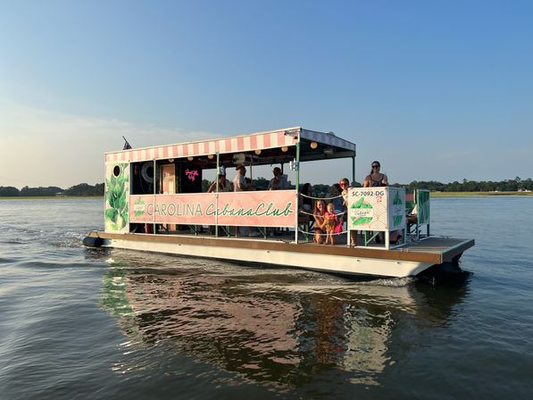 Pink-striped cabana-style pontoon boat with passengers enjoying a sunset cruise on calm coastal South Carolina waters