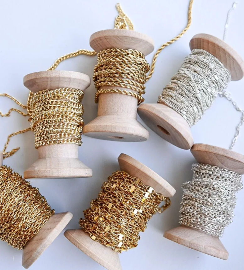 Wooden spools neatly wrapped with assorted gold and silver jewelry chains — sparkling trims for jewelry-making and craft projects.