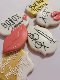 Botox-themed decorated sugar cookies with pink lips, syringe illustration and 'Botox' lettering on white and gold icing — cosmetic party favors