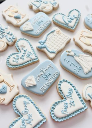 Assorted pastel blue and white iced sugar cookies styled for a bridal shower or engagement—heart shapes, diamond ring, wedding dress and calendar designs with 'something blue' messages on a white background.