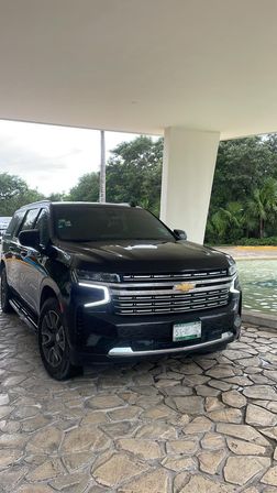 Sleek black Chevrolet SUV parked under a covered hotel entrance on a textured stone driveway beside a shallow reflecting pool and tropical palm trees