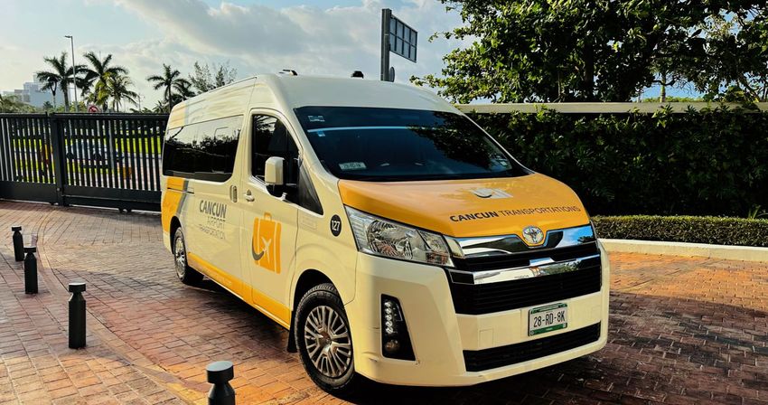 Yellow-and-white airport shuttle van parked on a brick driveway under palm trees on a sunny day in Cancun, Mexico