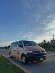 Orange-and-white airport shuttle van parked on a roadside in Cancun under a wide blue sky with wispy clouds and palm trees nearby.