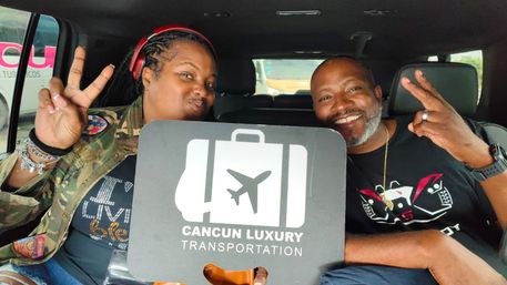 Smiling passengers in a car hold a suitcase-and-airplane logo sign for Cancun airport transportation while flashing peace signs