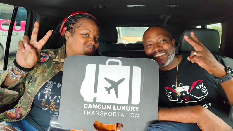 Smiling passengers in a car hold a suitcase-and-airplane logo sign for Cancun airport transportation while flashing peace signs