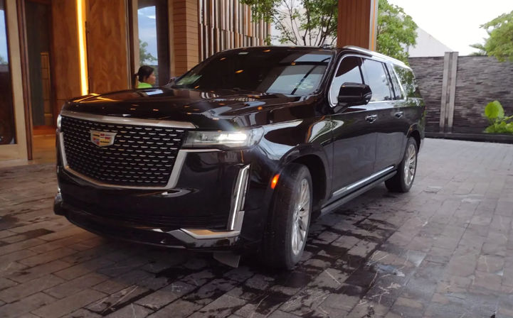 Luxury black SUV with Cadillac emblem parked at a hotel entrance on a wet stone driveway at dusk.