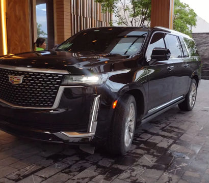 Luxury black SUV with Cadillac emblem parked at a hotel entrance on a wet stone driveway at dusk.