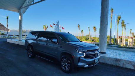 Sleek gray Chevrolet SUV parked under a resort porte-cochère beside a reflecting fountain, palm trees and international flags against a clear blue sky.