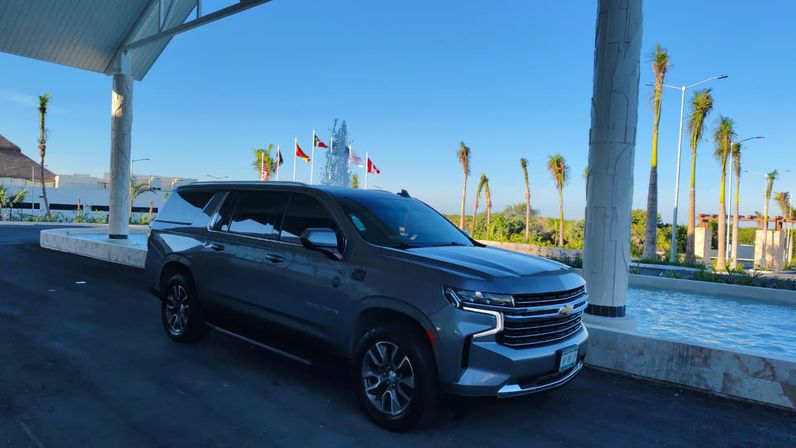 Sleek gray Chevrolet SUV parked under a resort porte-cochère beside a reflecting fountain, palm trees and international flags against a clear blue sky.