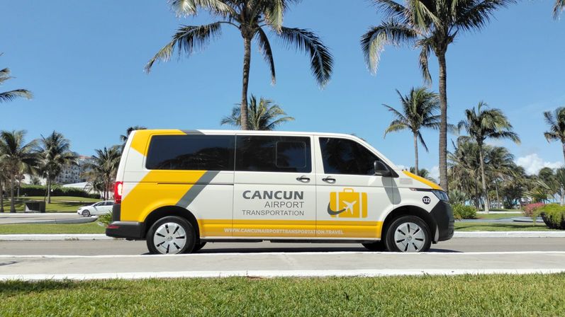 Yellow-and-white airport shuttle van on a palm-lined Cancún coastal road under a clear blue sky