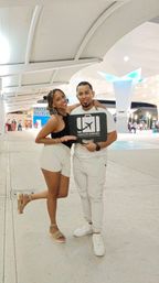 Smiling couple posing with an airport pickup sign in a modern Cancún airport terminal under illuminated canopy lighting