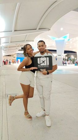 Smiling couple posing with an airport pickup sign in a modern Cancún airport terminal under illuminated canopy lighting