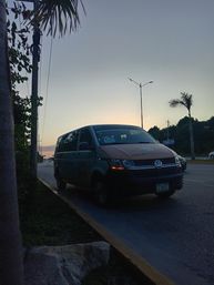 Sunset-lit Volkswagen shuttle van parked along a palm-lined Cancún road with streetlights and tropical foliage