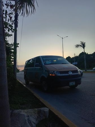 Sunset-lit Volkswagen shuttle van parked along a palm-lined Cancún road with streetlights and tropical foliage