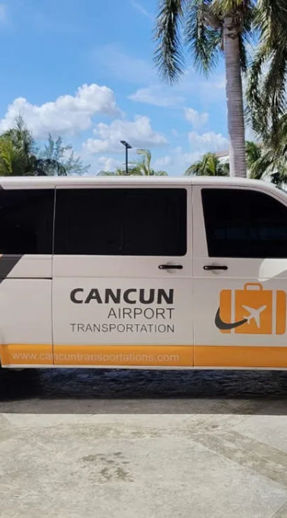 White-and-orange airport shuttle van with a luggage icon parked under palm trees at Cancun airport pickup area on a sunny day