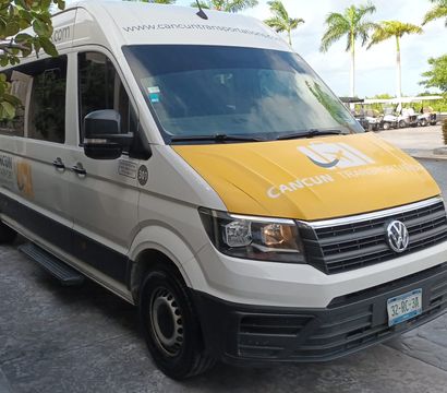 White-and-yellow airport shuttle van parked at a tropical Cancun resort drop-off with palm trees and golf carts in the background