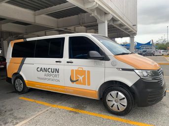 White-and-orange airport shuttle van with suitcase-and-airplane logo parked under a covered terminal at Cancun airport parking area