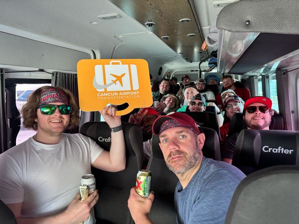 Group of cheerful adult travelers inside a Cancún airport shuttle van, holding drinks and a bright orange luggage sign for airport transfers