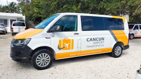 White-and-orange airport shuttle van parked on a gravel lot with palm trees, ready for Cancun airport transfers.