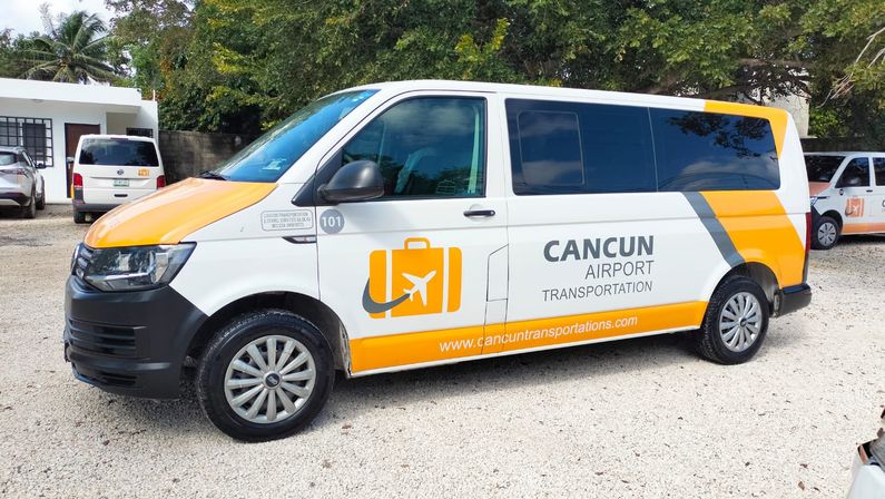 White-and-orange airport shuttle van parked on a gravel lot with palm trees, ready for Cancun airport transfers.