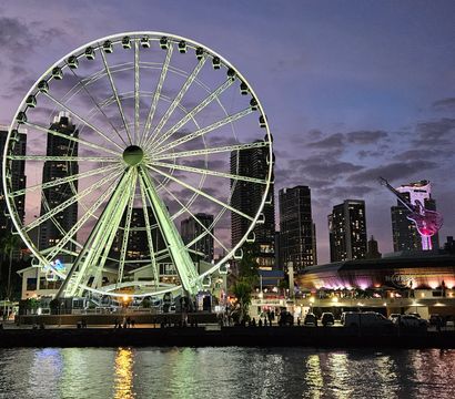 Illuminated waterfront Ferris wheel at dusk, colorful lights reflecting on the water with a downtown skyline and glowing guitar sculpture.