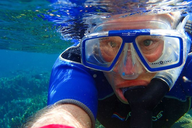 Close-up of a snorkeler in a blue mask and snorkel swimming in clear tropical blue water above a coral reef